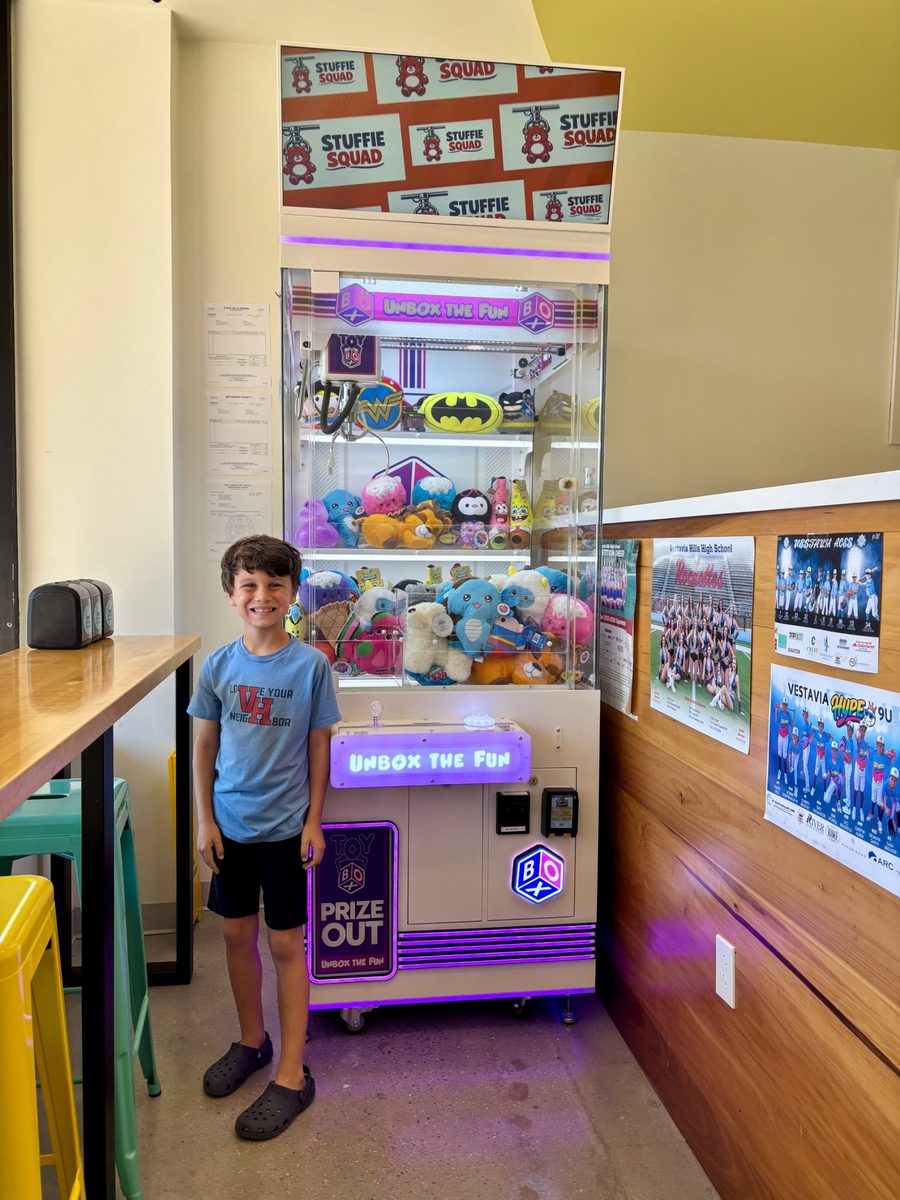 A smiling young player beside the Stuffie Squad claw machine at Sunshine Creamery